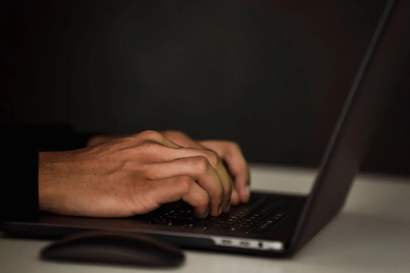 Mani che digitano su un portatile in penombra
