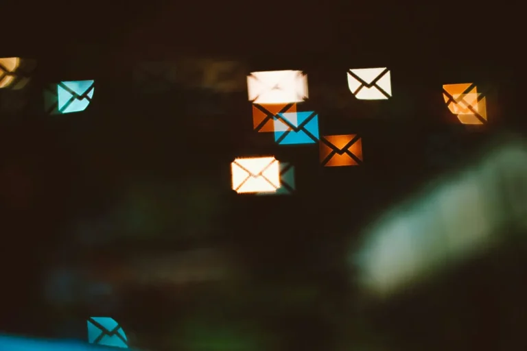 Luci sfocate a forma di busta blu, arancio e bianche su fondo scuro.
