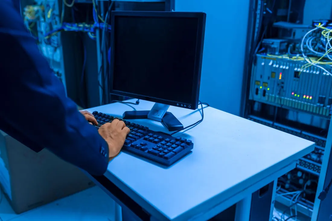 Tecnico di cui si vedono solo mani e braccio che usa una tastiera in una sala server illuminata di blu.