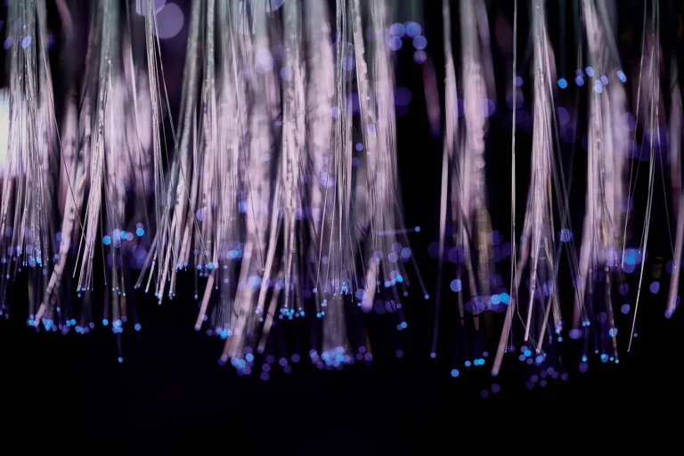 Fibre ottiche sottili e luminose viola e rosa con puntini di luce blu su sfondo nero.