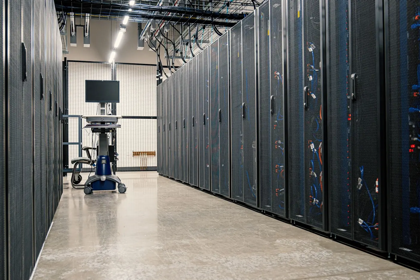 Corridoio di un data center con armadi server neri e un monitor su carrello in fondo.