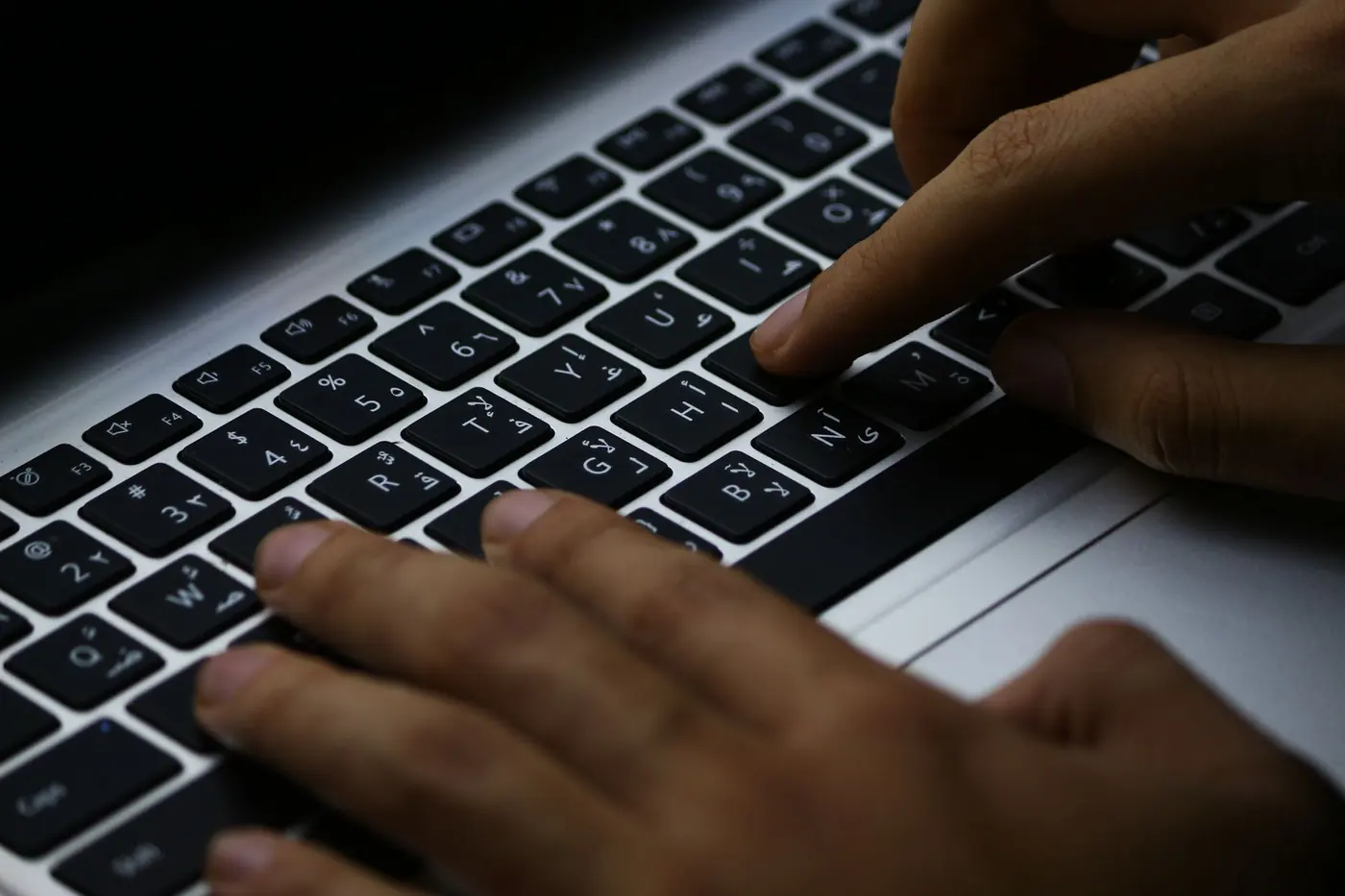 Mani che digitano su una tastiera di portatile in penombra.